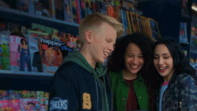 a boy is taking a selfie with two girls in front of a shelf of magazines including one called happiness