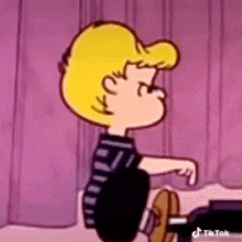 a cartoon of a boy with blonde hair and a black shirt is sitting on a bed .