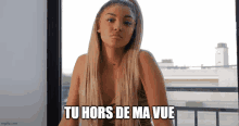 a woman is sitting in front of a window with the words tu hors de ma vue written on the bottom