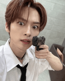 a young man in a white shirt and black tie is pointing a gun at the camera