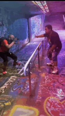 a man is taking a picture of another man on a skateboard in a tunnel with graffiti on the walls