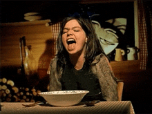 a woman sitting at a table with a bowl of cereal in front of her mouth