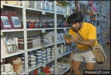 a man in a yellow shirt and shorts is standing in front of a shelf full of plates and cups .