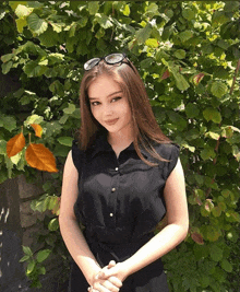 a woman in a black shirt and sunglasses stands in front of a bush