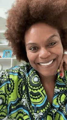 a woman with a big afro is smiling for the camera while wearing a green and blue shirt .