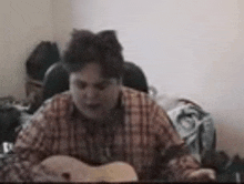 a man in a plaid shirt is playing an acoustic guitar in a room .