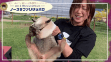 a woman is holding a small animal in her arms with a zoo and amusement space sign in the background