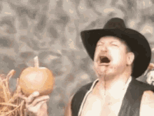 a man wearing a cowboy hat is holding a pumpkin with his mouth open