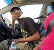 a man wearing glasses is sitting in the driver 's seat of a car next to a bottle of water