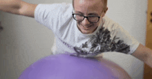 a man wearing glasses is holding a purple balloon .