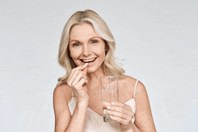 a woman is holding a glass of water and a pill in her mouth