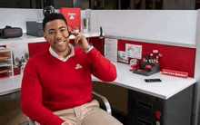 a man is sitting in an office cubicle talking on a cell phone .