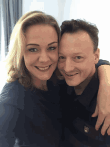 a man and a woman are posing for a picture and the man is wearing a black shirt with a shield on it