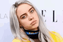 billie eilish wearing a yellow jacket and a blue scarf around her neck .