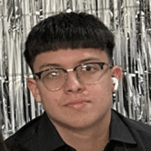 a young man wearing glasses and a black shirt is standing in front of a shiny background .