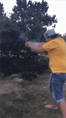 a man in a yellow shirt is holding a gun in front of a tree