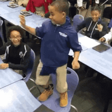 a boy in a blue shirt is standing on a chair in a classroom with other children .