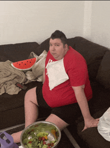 a man sitting on a couch with a bowl of salad on the table