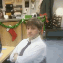 a man in a white shirt and tie is sitting at a desk in front of a christmas tree .