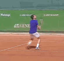 a man in a blue shirt is walking on a tennis court in front of a green wall that says general