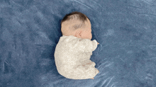 a baby is sleeping on a blue blanket and has a white outfit on