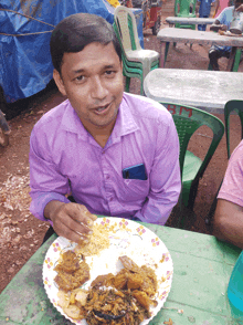 a man in a purple shirt sits at a table eating food