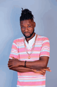 a man with dreadlocks is wearing a pink and white striped shirt and a gold chain around his neck .