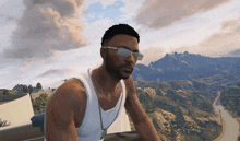 a man wearing sunglasses and a white tank top sits on a balcony overlooking a mountain