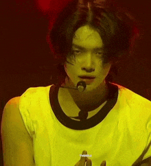 a young man with long hair is wearing a yellow shirt and a microphone on his neck .