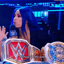 a woman with blue hair is talking into a microphone while holding a wrestling belt .