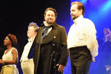 a group of people standing on a stage with one man wearing a black coat