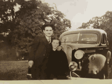 a black and white photo of a man and woman standing in front of an old car