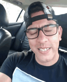 a man wearing glasses and a baseball cap is sitting in a car