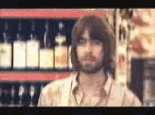 a man with long hair and a beard is standing in front of a shelf with bottles of alcohol .