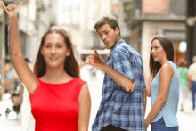 a man in a plaid shirt talks to a woman in a red dress while another woman looks on