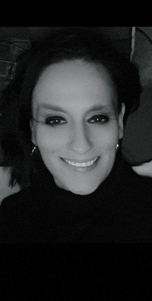 a woman wearing a black turtleneck and earrings is smiling in a black and white photo .