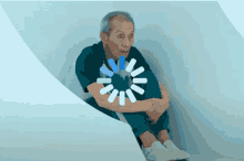 an elderly man sits in a room with a loading circle in the background