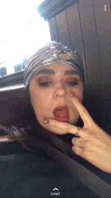 a woman wearing a turban and a ring is making a funny face with her finger on her face