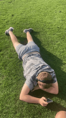 a young man is laying on his stomach on the grass looking at his phone