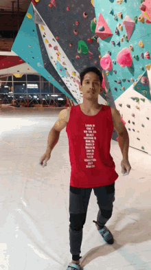 a man stands in front of a climbing wall wearing a red tank top that says ' london ' on the front