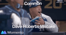 a man in a dodgers hat is sitting in the dugout with the words " common " and " dave roberts mistake " below him