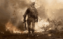 a soldier is walking through a field of fire with a gun .