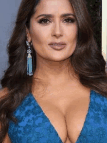 a woman in a blue dress with a plunging neckline and earrings .