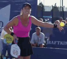 a woman in a pink tank top is holding a tennis ball and a paddle with the number 60 on it