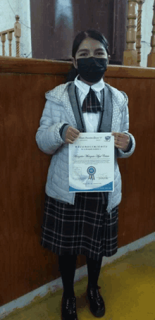 a young girl wearing a mask is holding a certificate of reconocimiento