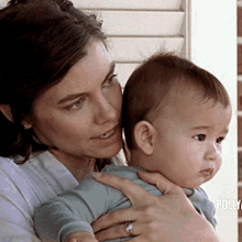 a woman is holding a baby in her arms and the baby is wearing a blue shirt and a ring on her finger