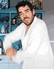 a man with a beard is wearing a white shirt and dancing in front of a blue dresser .