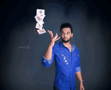 a man in a blue shirt is throwing playing cards in the air and the photo was taken by jimmy singh