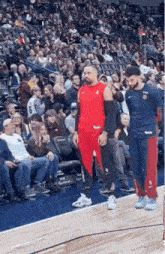 a man in a red shirt and red pants is standing on a basketball court in front of a crowd .