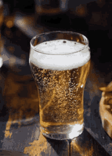 a glass of beer is sitting on a wooden table next to a plate of french fries